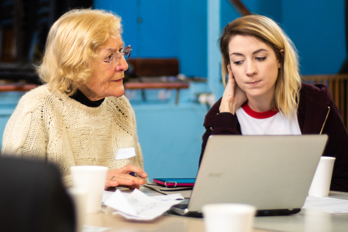 A woman in later life being taught to use a computer by a younger person