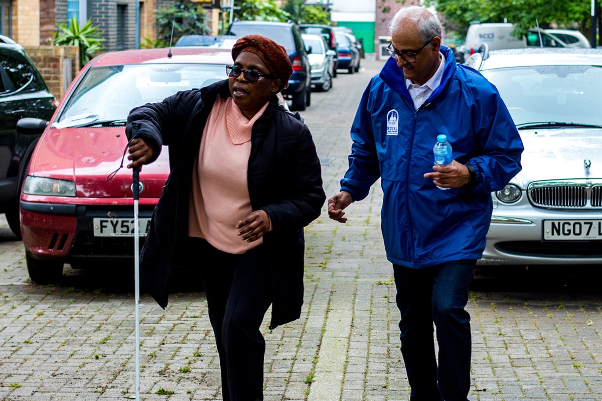 Indian male volunteer, helping disabled black woman down the street.