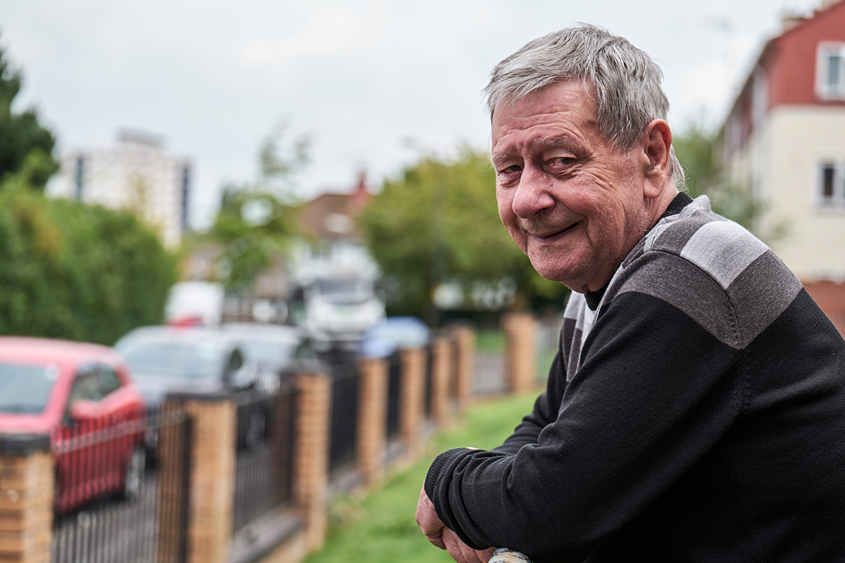 Older man looking into camera, leaning on fence