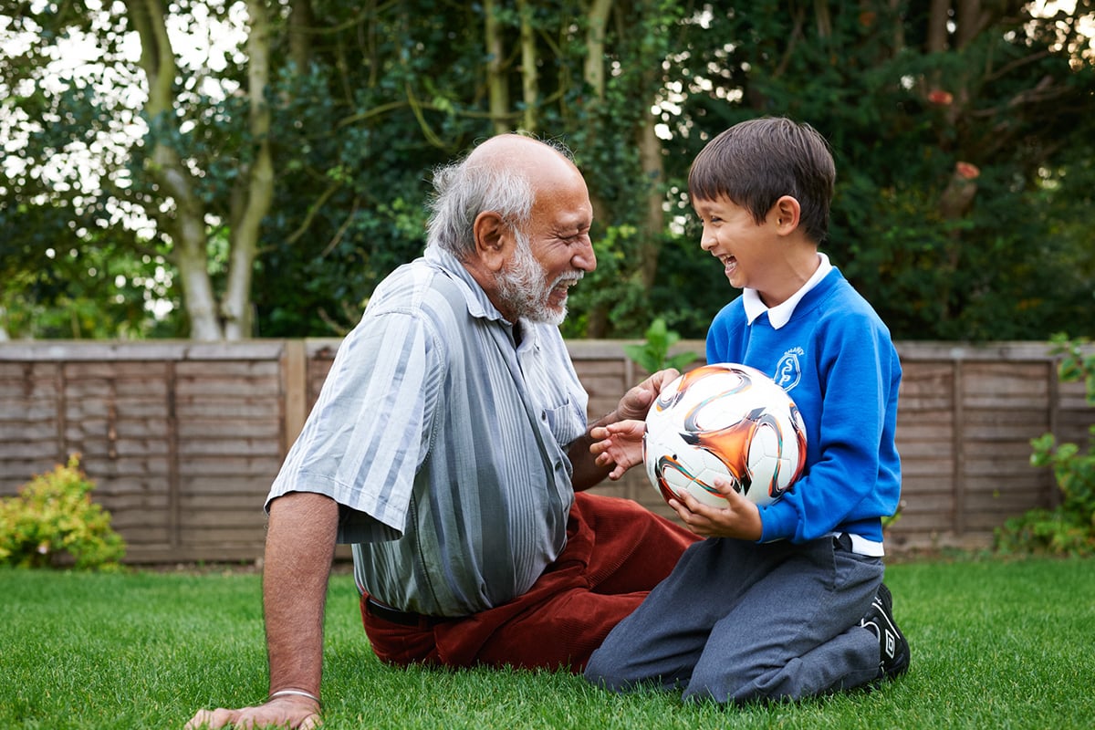 Elderly man and grandson sitting on grass with football.