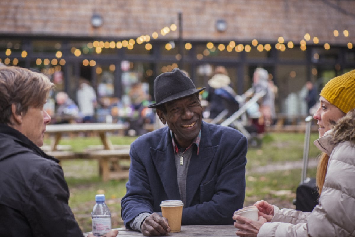 Three older adults from different ethnicities sit around a table outside at a cafe