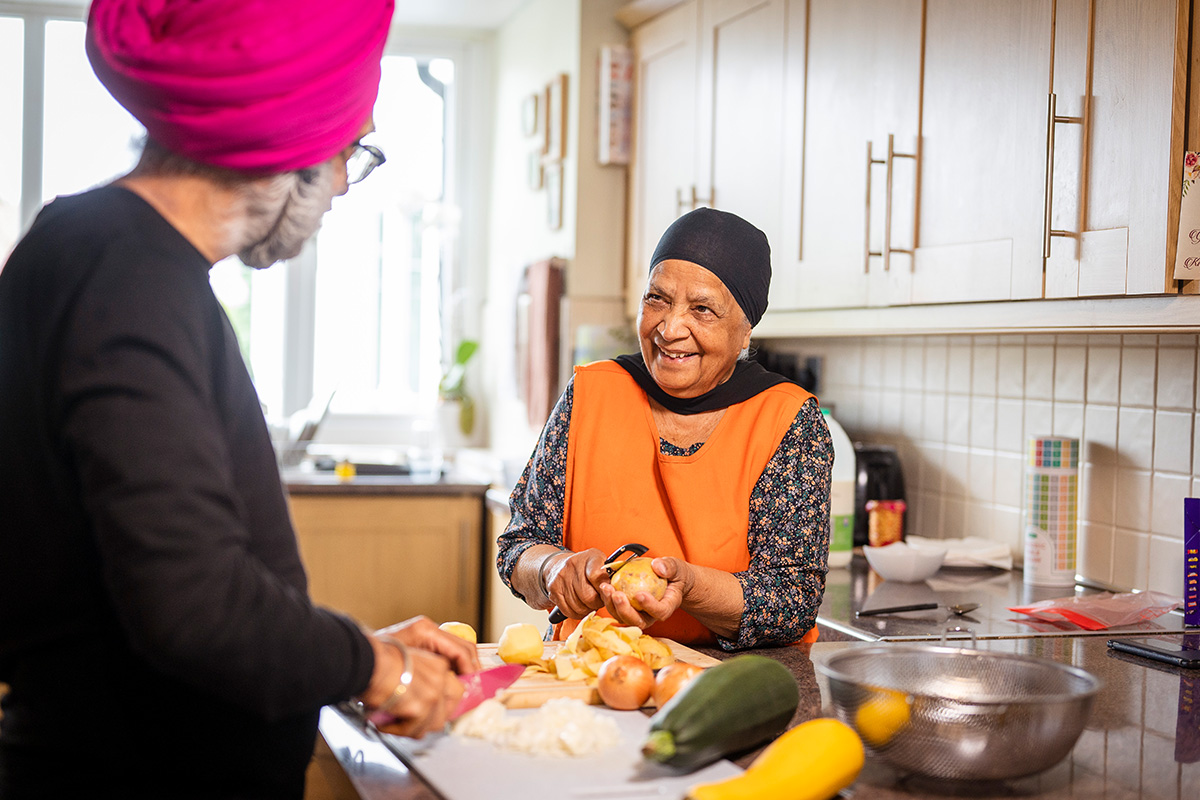older woman chatting with a man while chopping vegetables