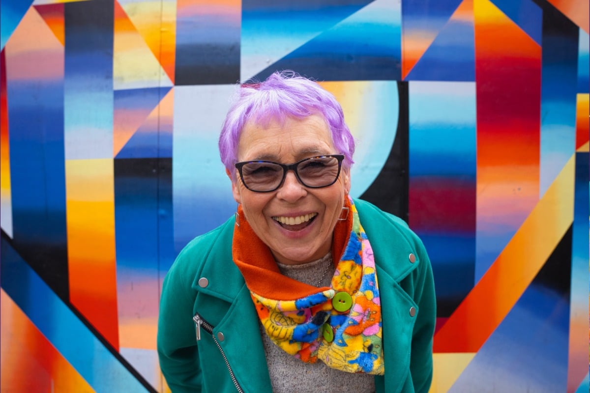 Older woman with purple hair smiling into the camera