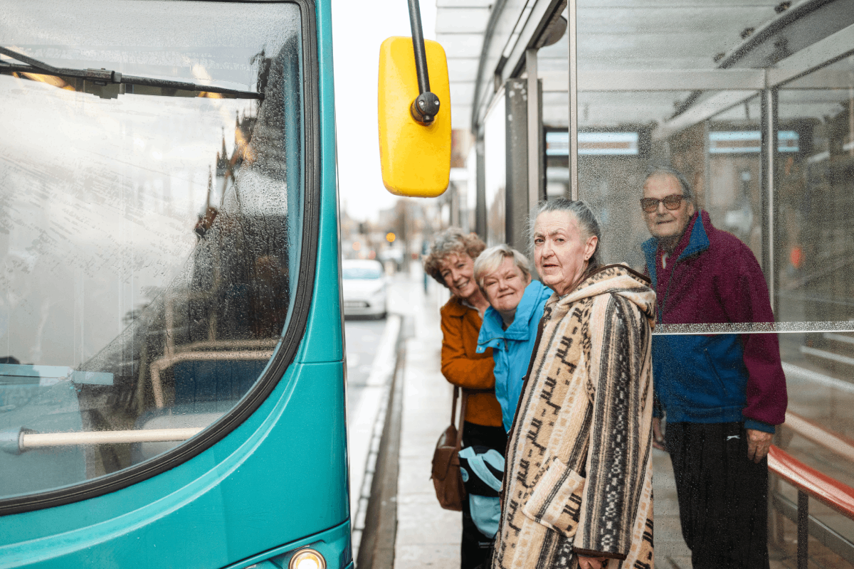 A group of older adults stand at a bus stop waiting to board the bus