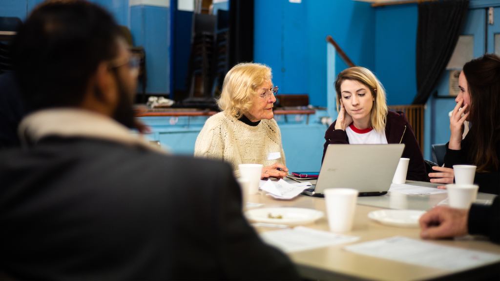A woman in later life being taught to use a computer by a younger person