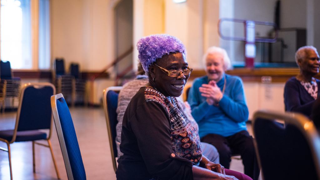 Elderly people sitting in a circle of chairs doing a gentle exercise class.