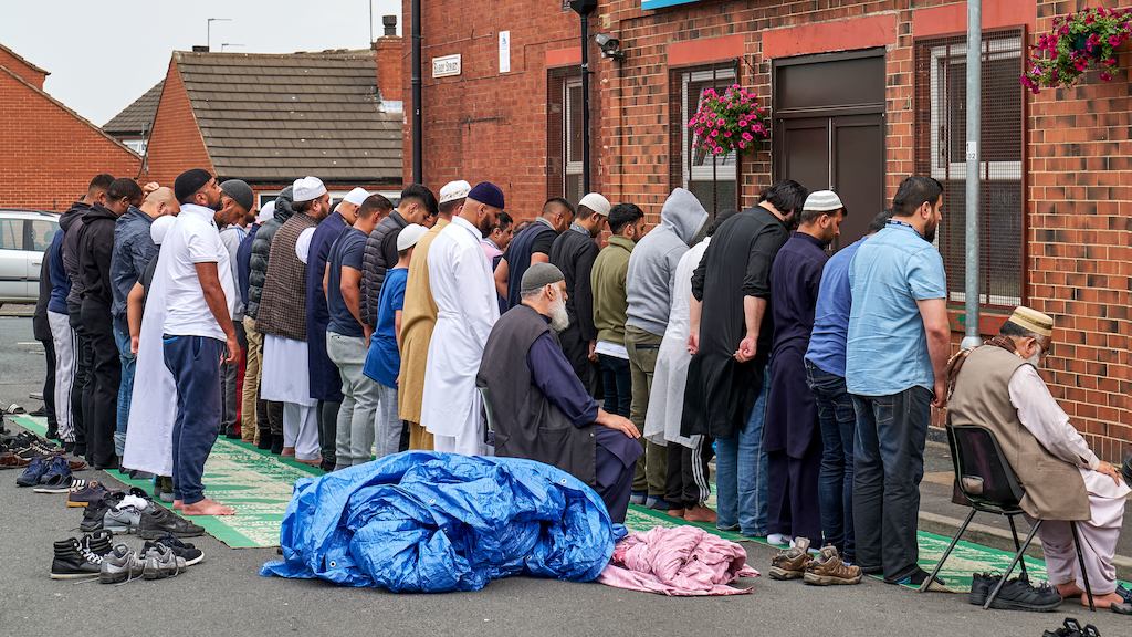 Group of Muslim men praying outside a building.