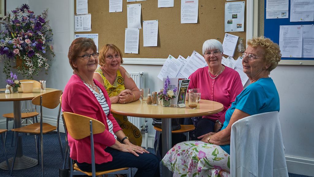 Four elderly ladies sitting around a table smiling.