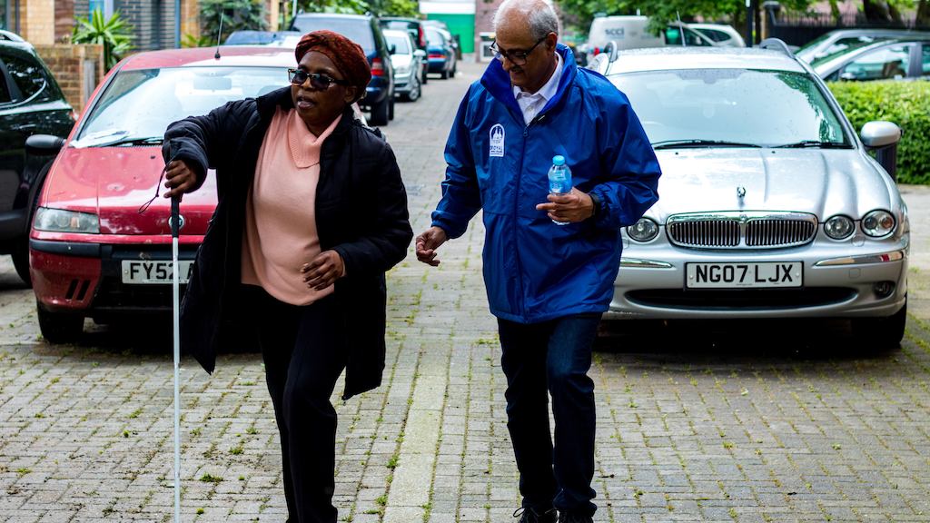 Indian make volunteer, helping disabled black woman down the street.