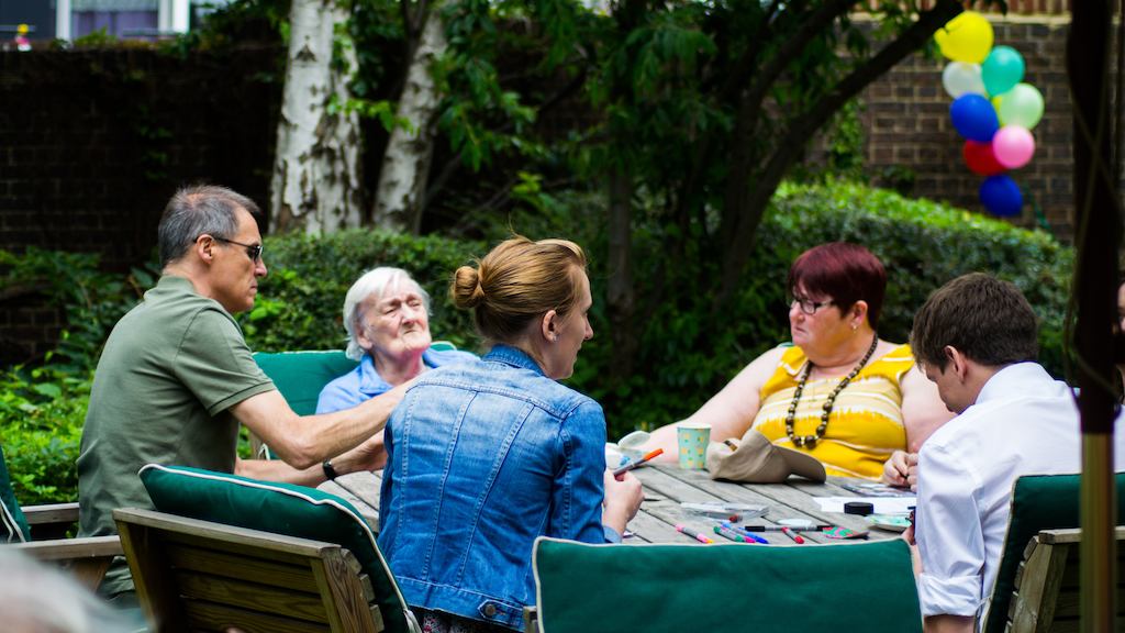 Small group of old and young people sitting at a table outside.