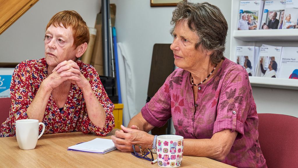Two older women seated at a table.