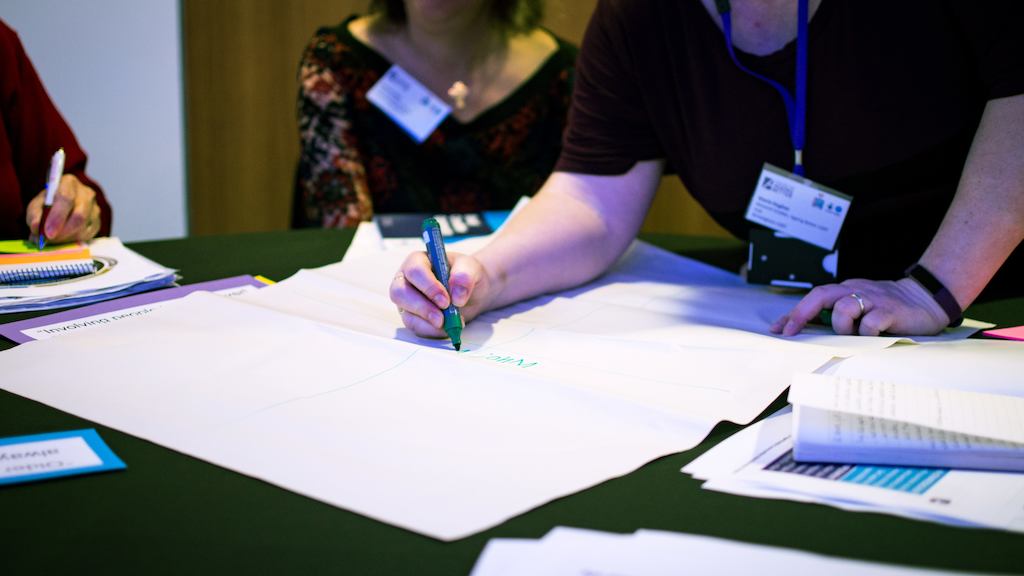 People brainstorming with pens and paper at a conference.