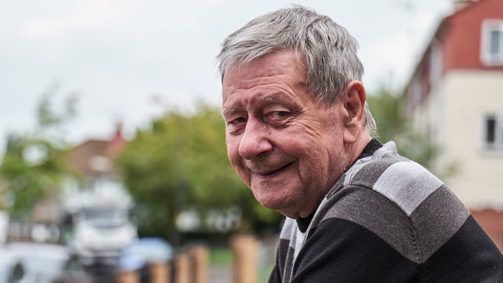 Older man looking into camera, leaning on fence