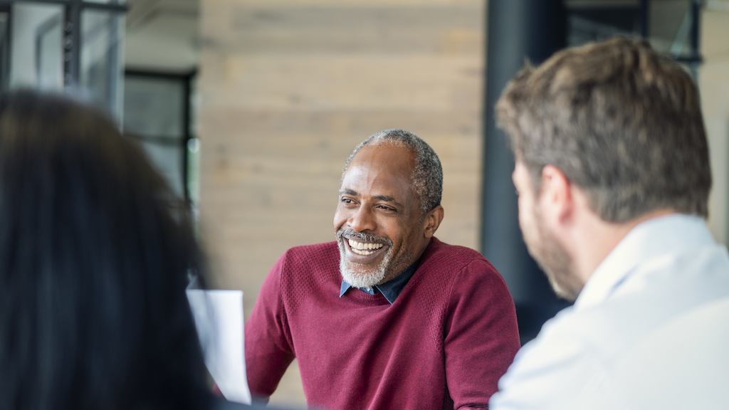 Smiling mature male manager sitting with colleagues in board room. Multi-ethnic professionals are planning strategy during meeting. They are at new office.