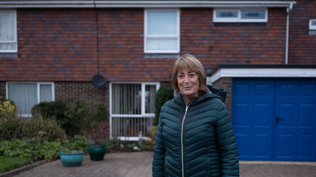 an older woman standing on the driveway of her house