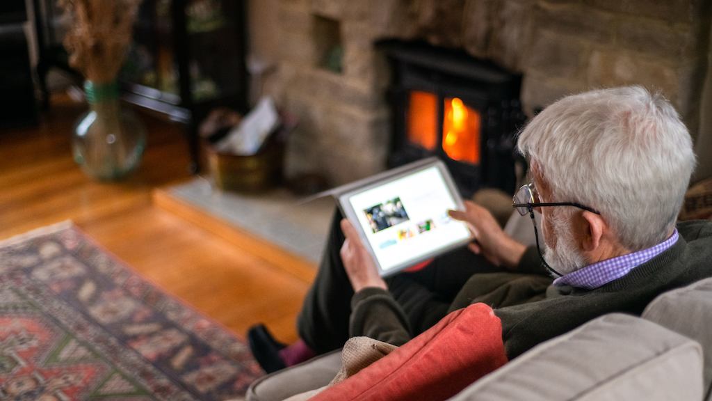 Older man sat on his sofa browsing the internet on his tablet