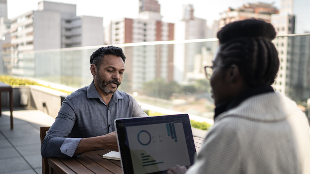 Two office employees sit outside, working together
