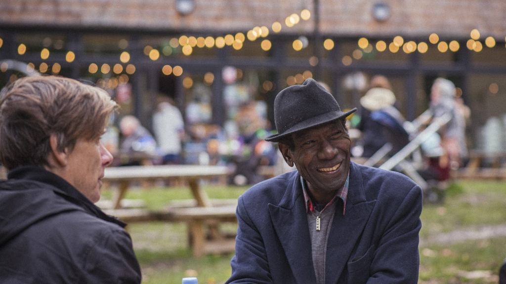 Two older adults from different ethnicities sit around a table outside at a cafe