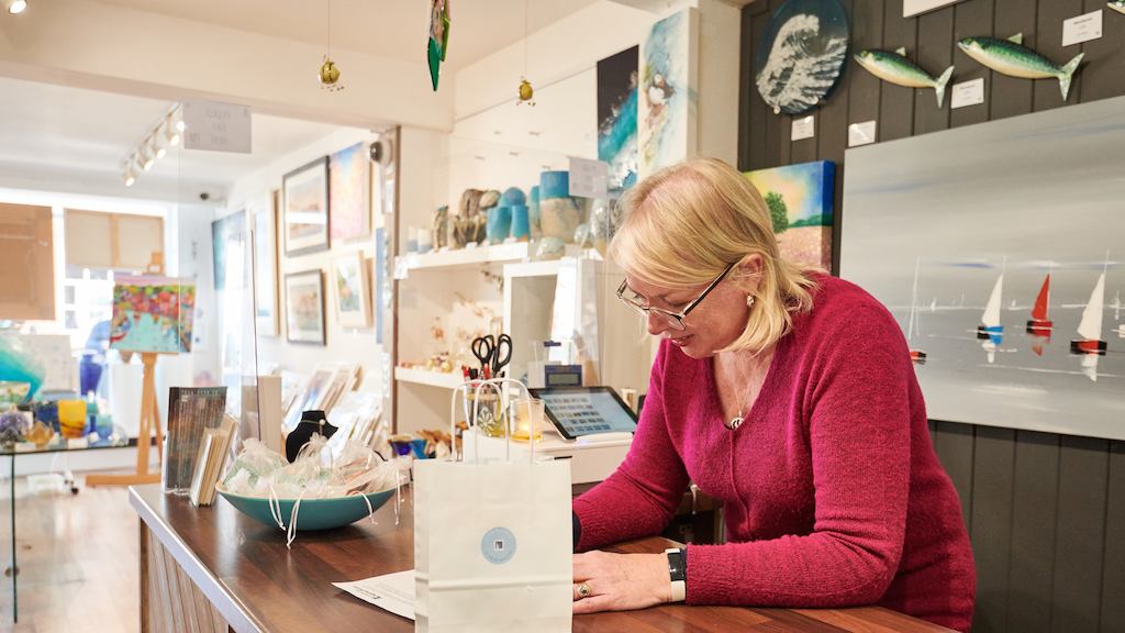 older woman filling out a form behind a till
