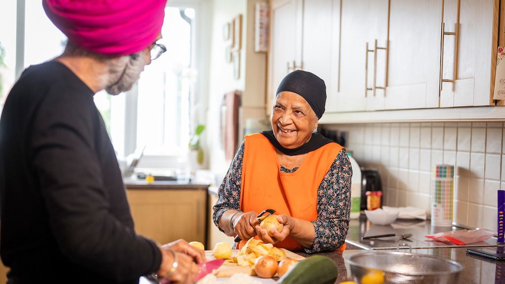 older woman chatting with a man while chopping vegetables
