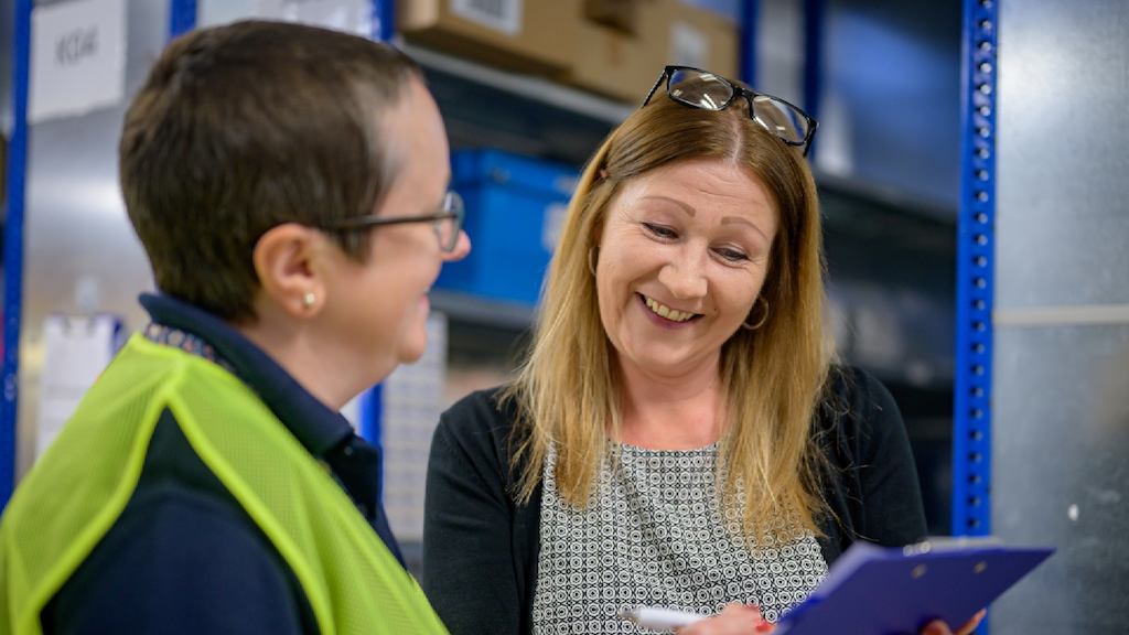two older women writing on a clip board and talking 
