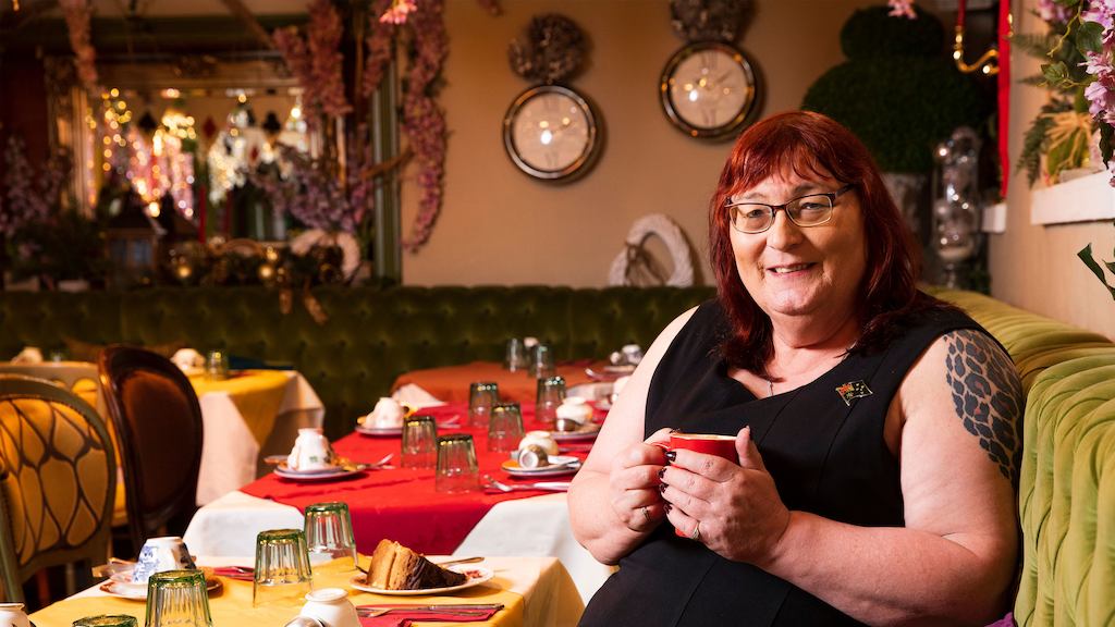 Rachel, sitting down in a cafe with a cup of tea, smiling at the camera