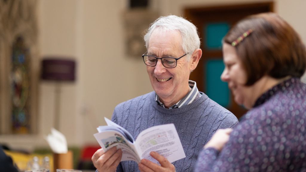 An older man chatting whttps://ageing-better.org.uk/sites/default/files/media/image_hero/images/2023-02/why-being-an-age-3840x2160.jpgith a woman reading a book