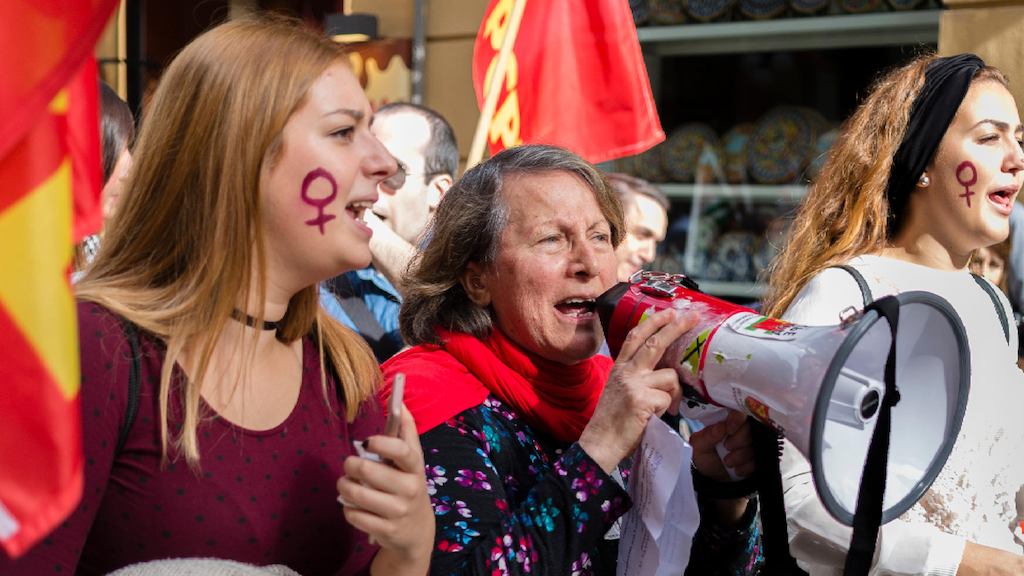 An image of three women with flags and loudspeakers taking part in a protest