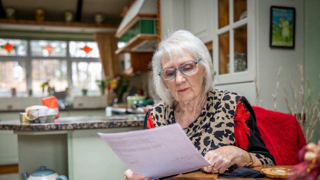 A woman wearing glasses reads a document in her kitchen