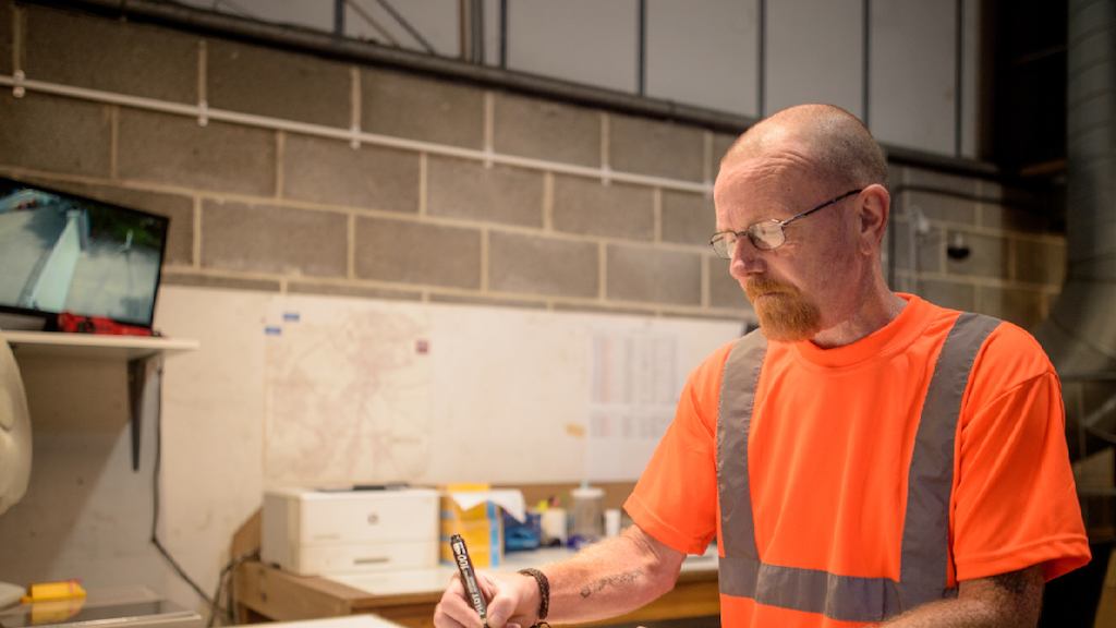 An older male worker in a hi-vis orange jacket seals up a cardboard box