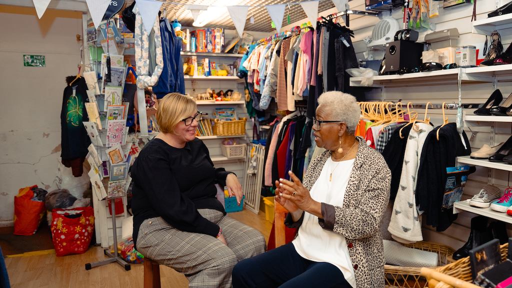 Two older women sitting in a charity shop talking