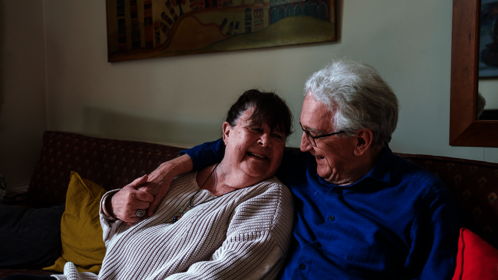 An older couple embrace on a sofa