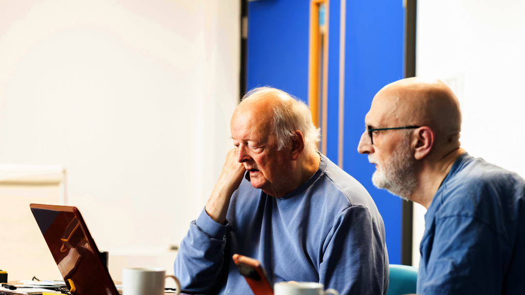 Two older men look at a laptop together