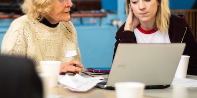 A woman in later life being taught to use a computer by a younger person