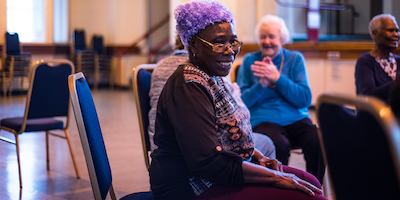Elderly people sitting in a circle of chairs doing a gentle exercise class.