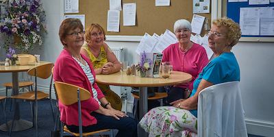 Four elderly ladies sitting around a table smiling.