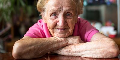 Elderly woman in pink t-shirt resting her chin on crossed arms.