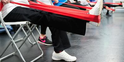 Women seated in exercise class using stretch bands on their legs.