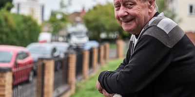 Older man looking into camera, leaning on fence