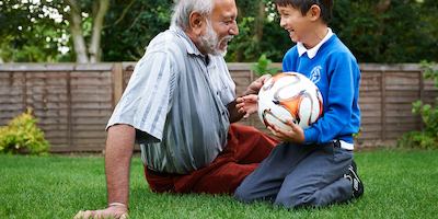Elderly man and grandson sitting on grass with football.
