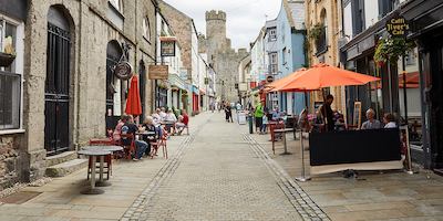 view down a paved street lined with shops and cafes with people seated outside