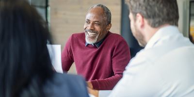Smiling mature male manager sitting with colleagues in board room. Multi-ethnic professionals are planning strategy during meeting. They are at new office.