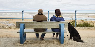 an older couple with their dog, sitting on a bench looking out to sea