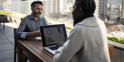 Two office employees sit outside, working together