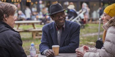 Three older adults from different ethnicities sit around a table outside at a cafe