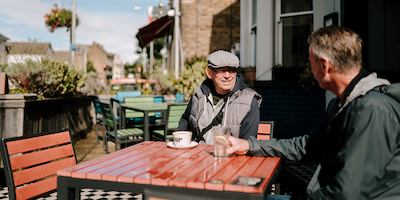 Two older men sitting by a table outside