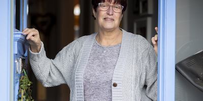 older women looking out from her front door