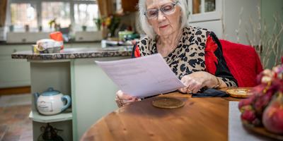 A woman wearing glasses reads a document in her home