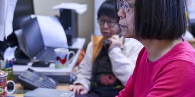 Two women of different ethnicities use computers in an office