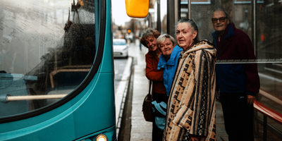 A group of older adults stand at a bus stop waiting to board the bus